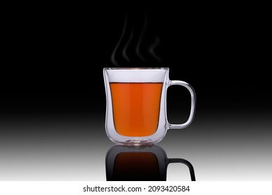 Double glass cup of tea on a black background. Double glass cup isolated. Modern glass tea cup. Steam over a glass cup of tea on the mirror.