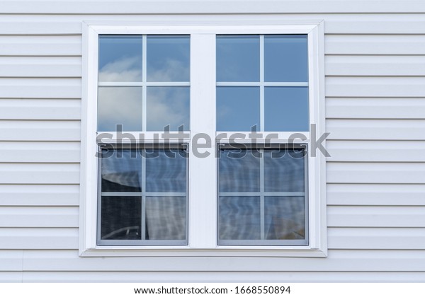 Double hung window with fixed top sash and\
bottom sash that slides up, sash divided by white grilles a\
surrounded by white elegant frame  horizontal white vinyl siding on\
a new construction\
residence