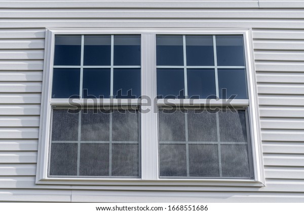 Double hung window with fixed top sash and\
bottom sash that slides up, sash divided by two white grilles,\
surrounded by white elegant frame  horizontal white vinyl siding on\
new residence