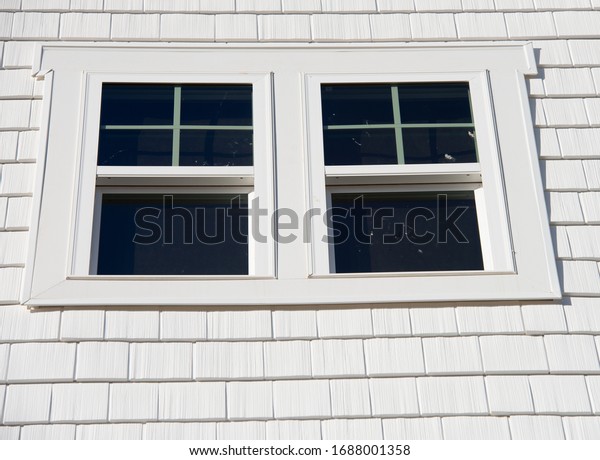 Double hung window with fixed top sash and\
bottom sash that slides up, sash divided by white grilles a\
surrounded by white elegant frame  horizontal white shingle siding\
on new construction\
residence