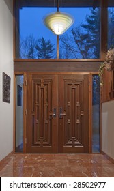 Double Mahogany Front Doors Leading To A Marble Foyer Shot At Dusk