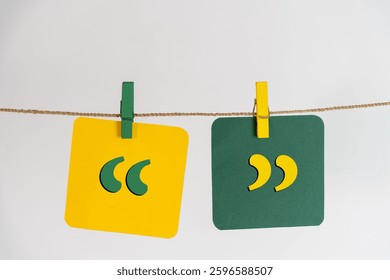 Double quotation marks printed on yellow and green papers, hanging on a rope, representing speech and communication, emphasis and irony, or quoting and referencing