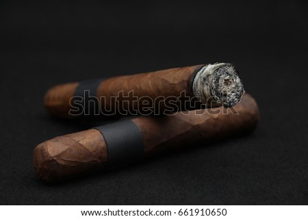 Double robusto cigars with dark wrapper on black background.