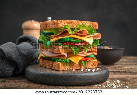 Double sandwich with ham, cheese and fresh vegetables on a wooden board on a brown background. Side view, close-up.