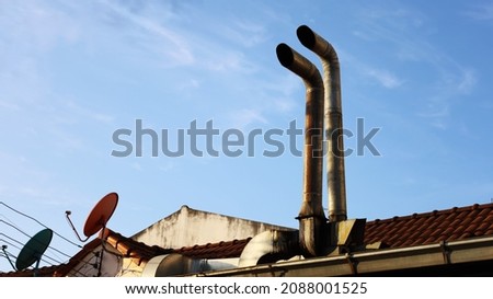 Double ventilation pipes on the roof. Old rusty metal exhaust pipe with satellite dish on the roof and a sunny afternoon blue sky background with copy space. Selective focus