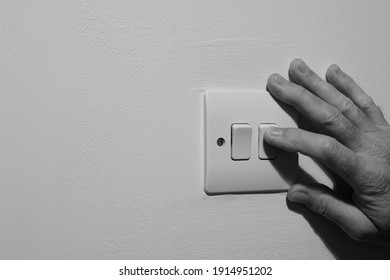 A Double Wall Light Switch, Showing A Natural Elderly Hand Switching Off The Power Supply To Save Electricity In The UK.