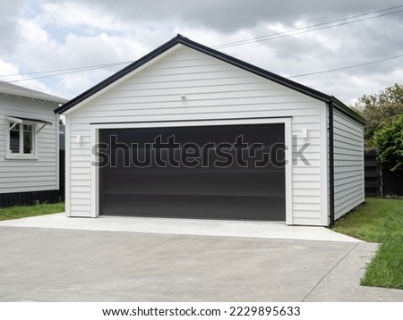 Double white garage with gable roof and black tilt-up retractable raised panel metal door