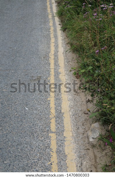 Double yellow lines\
from an edge of an uphill road. Double yellow lines from a road in\
Cornwall, England.