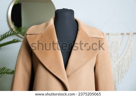 Double-breasted coat in double camel fabric with a wide collar. Demonstration of clothing on a tailor's mannequin. Detail of demi-season outerwear.