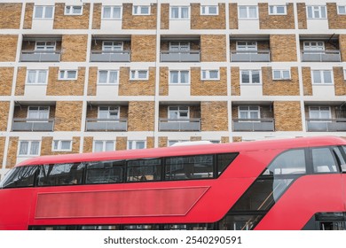 A double-decker bus passing in front of a brick and white apartment building on Collingwood, Estate in London