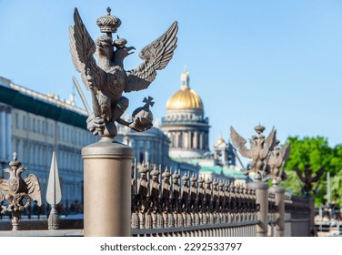 Double-headed eagle on the fence of the Alexander Column at the Winter Palace and a view of St. Isaac's Cathedral (blurred focus), St. Petersburg, Russia