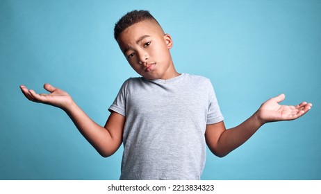 .Doubt, Question And Shrug From Child With Confused Facial Expression, Dont Know Gesture And Raised Hands. Young Boy, African Youth And Face Portrait Of Puzzled Black Kid Isolated On Blue Background.