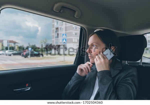 Doubtful businesswoman\
talking on mobile phone on car back seat, business on the move\
concept. Elegant adult caucasian female person using smartphone for\
communication.