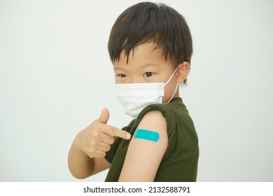 Doubtful Child After Getting A Vaccine. Little Kid Wearing Medical Mask Showing His Arm With Bandage After Receiving Vaccination, COVID 19 Vaccine For Children And Youth, Back To School Concept