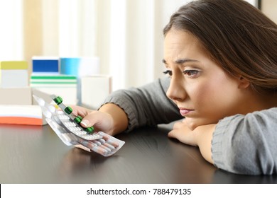 Doubtful woman looking to a lot of medicines sitting in a table at home