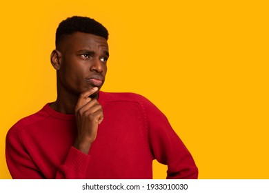 Doubtful Young Black Man Looking Aside At Copy Space With Curiousity. Unsure African Guy Touching Chin, Thinking About Interesting Offer While Standing Isolated Over Yellow Background, Panorama