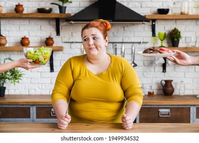 Doubting caucasian fat plus size woman choosing between healthy salad and junk sweet food donuts in the kitchen. Healthy dieting and bulimia concept