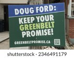 doug ford keep your greenbelt promise sign on wood post in front of residential homes, green blue white rectangle sign