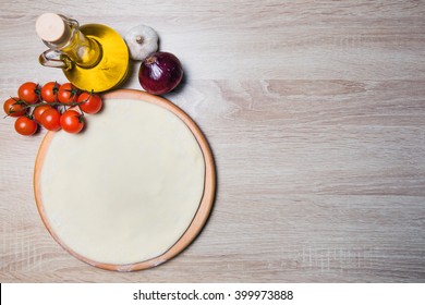 Dough basis for the pizza on a wooden board and cherry tomatoes, olive oil, onions, garlic.