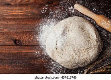 Dough with flour, rolling pin and wheat ears on rustic wooden table from above. Homemade pastry for bread or pizza. Bakery background - Powered by Shutterstock