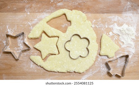 from dough lying on a wooden surface dusted with flour, cookie cutters pressed into star, christmas tree, and flower shapes, homemade baking, cooking at home from scratch - Powered by Shutterstock