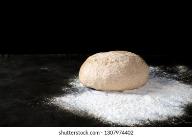 Dough with spilled flour on a black background. Yeast dough for bread, rolls, pizza, focaccia or pie. Cooking healthy bread from wholegrain flour. Copy space.