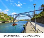 Douro river with traditional sailing wine boat cruise, view of Maria Pia and Sao Joao bridges, typical architecture of cascade housing in sunhine, Porto, Portugal
