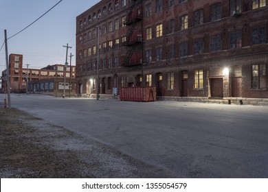 Down an industrial street behind a vintage multiple story red brick blue collar warehouse with lights in a depressed urban area of St. Louis Missouri - Powered by Shutterstock