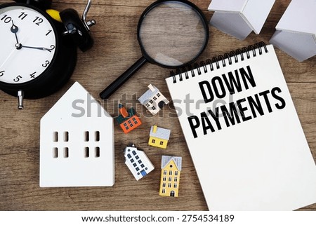 Down Payments text written on notepad with house model, magnifying glass and alarm clock on wooden background