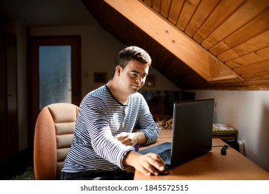 Down syndrome adult man sitting indoors in bedroom at home, using laptop.