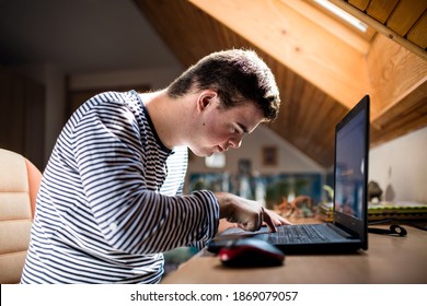 Down syndrome adult man sitting indoors in bedroom at home, using laptop.