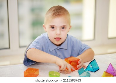 Down syndrome boy, trisomy on chromosome 21, chromosome disorder, genetic disease, child playing with plastic geometric figures, teaching special children.
