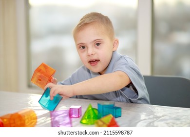 Down syndrome boy, trisomy on chromosome 21, chromosome disorder, genetic disease, child playing with plastic geometric figures, teaching special children.
