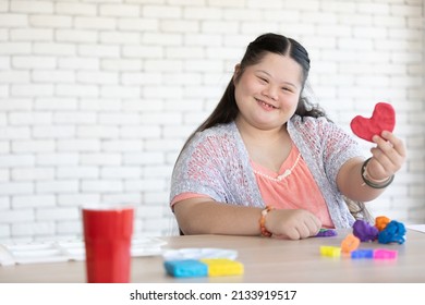down syndrome girl sculpt and looking red heart plasticine and learning to use colorful play dough on a table