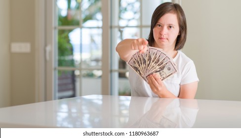 Down syndrome woman at home holding dollars pointing with finger to the camera and to you, hand sign, positive and confident gesture from the front Stock Photo