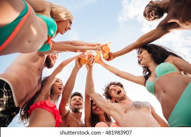 Down view image of a group of happy friends clinking beer bottles standing together in swimwear