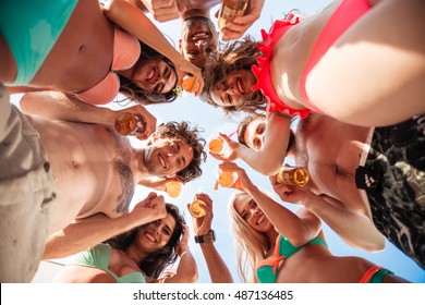 Down view image of a group of happy friends clinking beer bottles standing together in swimwear