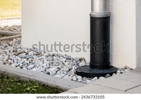 Downspout or Downpipe into French Drain Stones Floor Around Wall Building Outside. Modern Drainage System for Stormwater or Rainwater with Gravel Stones Covering by House Wall.