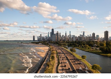 Downtown Chicago city skyline aerial centered over traffic along Lake Shore Drive between South Lagoon and Lake Michigan on a sunny day with fluffy white clouds in a blue sky above.
