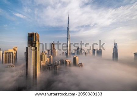 Downtown Dubai with skyscrapers submerged in think fog. Picture taken from unique view. Tall buildings. Early morning glow. 