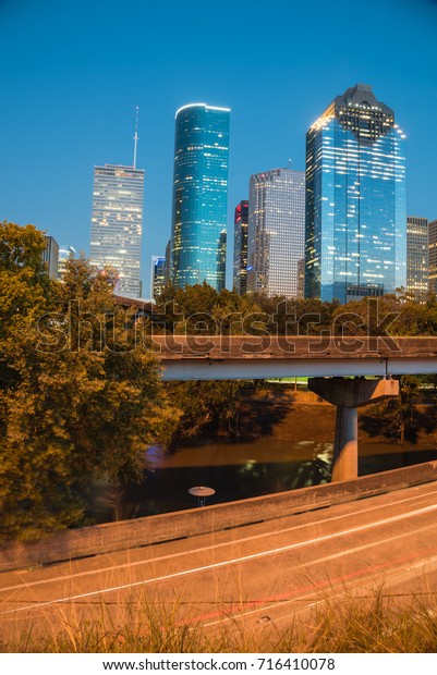 Downtown Houston from Buffalo Bayou Park at blue\
hour. Highway car light trails in front and skyscrapers from\
central business district in background. Transportation,\
architecture and travel\
concept
