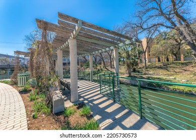 Downtown San Antonio, Texas- River walk with arbor on concrete path beside the river. There is an pergola roof with dried vines and railings between the pathway and the river.