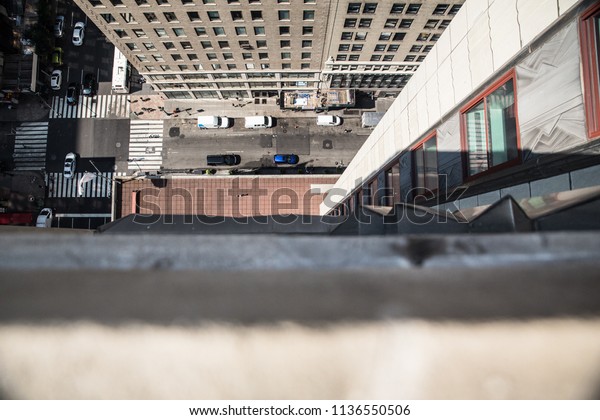 Downwards view from the ledge of a building\
in New York City with street below in\
view