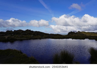 Doxey Pool at The Roaches, Peak District, offers a scenic view of a natural pond surrounded by rugged rock formations. Captured under a blue sky with reflections on the water. - Powered by Shutterstock