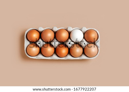 A dozen eggs in a box on the table with one white egg, top view. Minimalistic product concept
