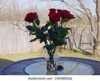 A Dozen Long-stemmed Red Roses In A Glass Vase On A Table Outdoors In Winter