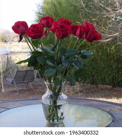 A Dozen Long-stemmed Red Roses In A Glass Vase On A Table Outdoors