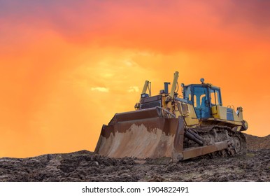 Dozer on earthmoving at construction site on sunset background. Construction machinery and equipment on groundwork. Bulldozer leveling ground in open pit. Mining industry concept