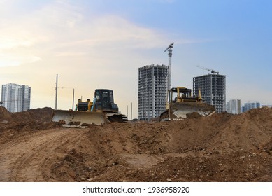 Dozer on earthmoving at construction site on sunset background. Construction machinery and equipment on groundwork. Bulldozer leveling ground for new road construction. Tower cranes in action