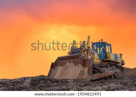 Dozer on earthmoving at construction site on sunset background. Construction machinery and equipment on groundwork. Bulldozer leveling ground in open pit. Mining industry concept